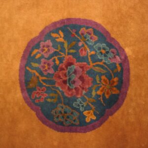 Orange rug detail showing a round teal medallion framed in purple with multicolored floral motifs.