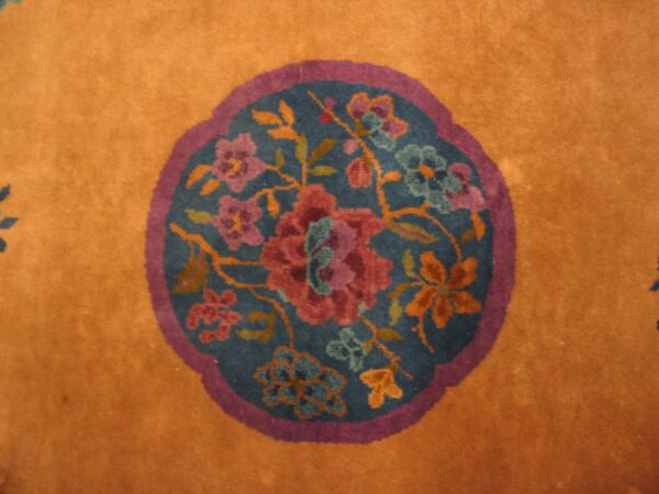 Orange rug detail showing a round teal medallion framed in purple with multicolored floral motifs.
