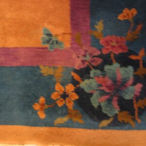 Detail of a rug showing orange, purple, and teal borders framing colorful floral designs and a butterfly.