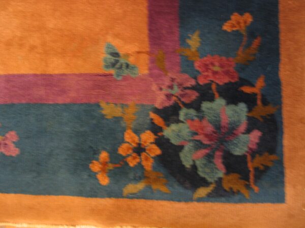 Detail of a rug showing orange, purple, and teal borders framing colorful floral designs and a butterfly.