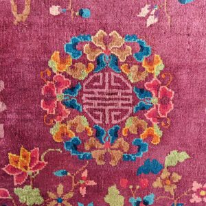 Vivid close-up of a magenta rug with multicolored floral elements and a central geometric design.