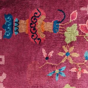 Close-up of a magenta rug featuring stylized floral and abstract motifs in blue, green, coral, and orange colors.