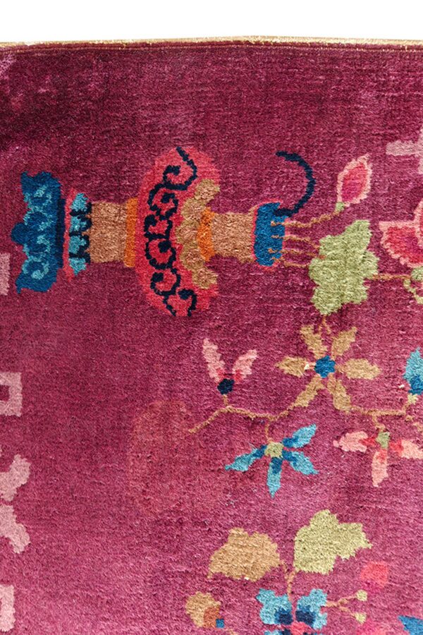 Close-up of a magenta rug featuring stylized floral and abstract motifs in blue, green, coral, and orange colors.