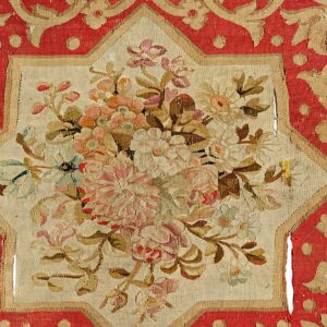 Flatweave rug fragment in red and tan features a center bouquet of pink and green stylized flowers.