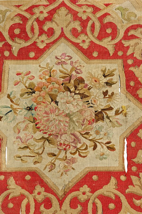 Flatweave rug fragment in red and tan features a center bouquet of pink and green stylized flowers.