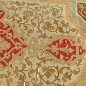 Detailed flatweave rug fragment featuring red, tan, and brown scrolling botanical designs with noticeable wear.