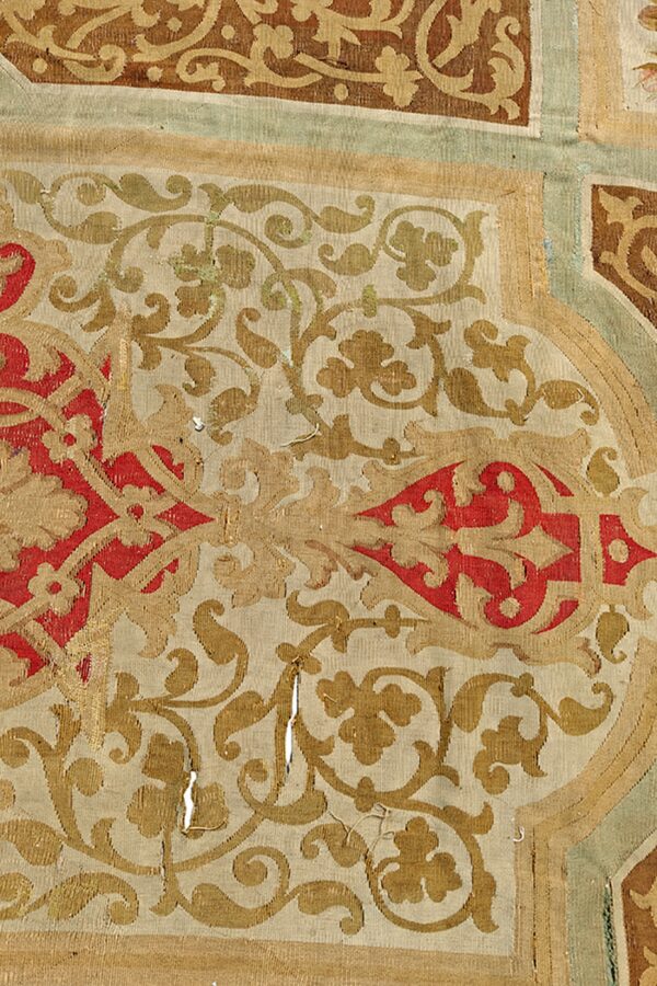 Detailed flatweave rug fragment featuring red, tan, and brown scrolling botanical designs with noticeable wear.