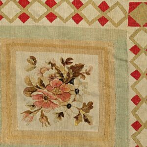 Flatweave rug detail with a central floral bouquet panel framed by green, tan, and red geometric borders.