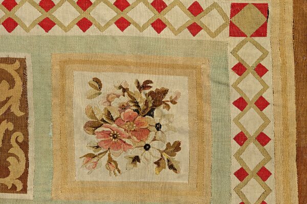 Flatweave rug detail with a central floral bouquet panel framed by green, tan, and red geometric borders.