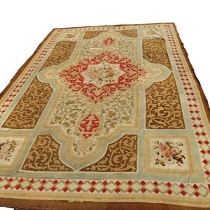 Ornate low pile rug featuring complex scrollwork in brown, red, cream, and pale aqua green colors.