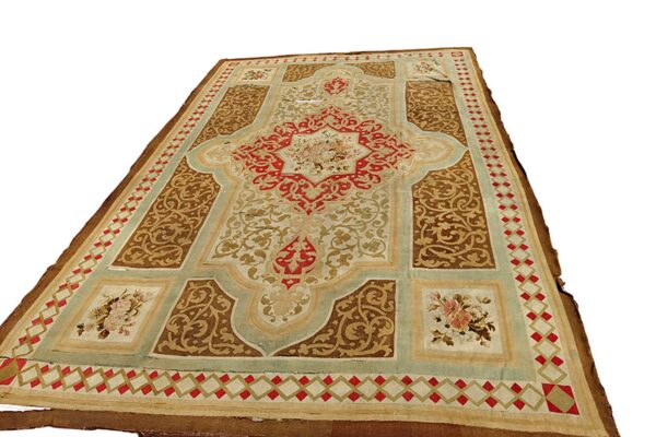 Ornate low pile rug featuring complex scrollwork in brown, red, cream, and pale aqua green colors.
