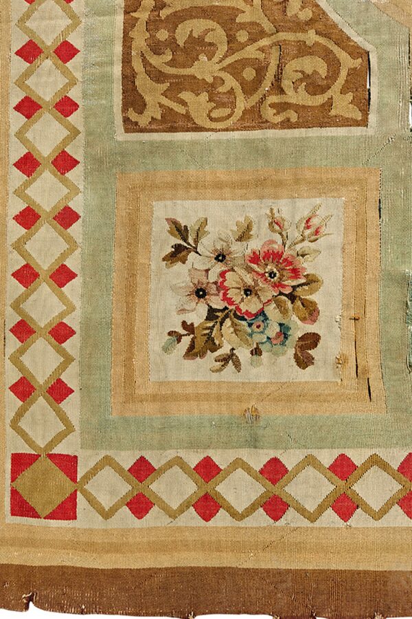 Section of a flatwoven rug displaying red diamonds, tan scrollwork, and a central panel of colored flowers.