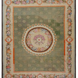 Distressed sage green rug featuring a central floral medallion and a wide cream border with colorful flowering vines.