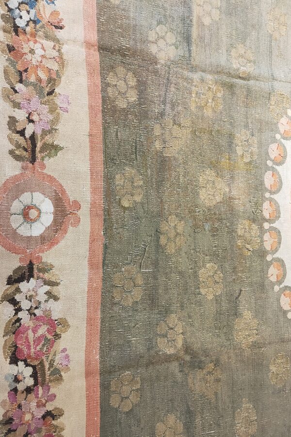 Muted sage rug field with khaki flowers and a cream border featuring detailed pink, blue, and green floral motifs.