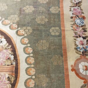 Close-up of a low-pile rug with a faded sage green field, beige floral motifs, and a multicolored floral border.