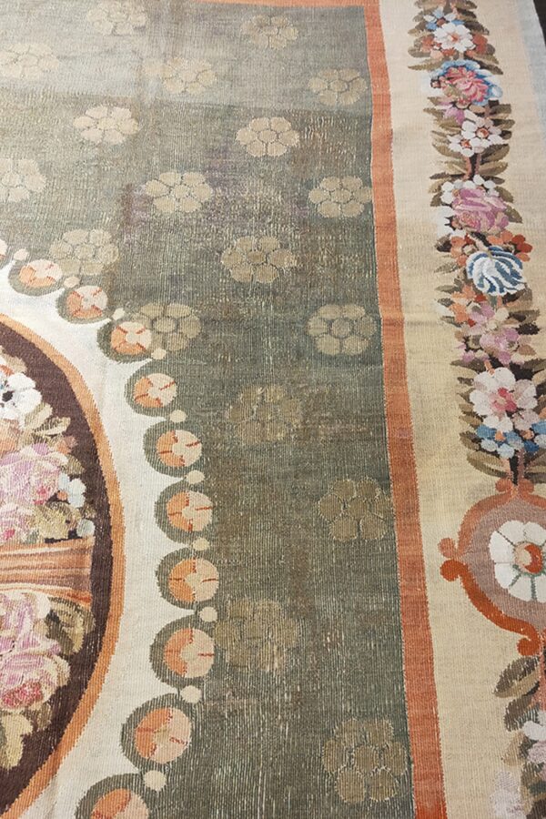 Close-up of a low-pile rug with a faded sage green field, beige floral motifs, and a multicolored floral border.