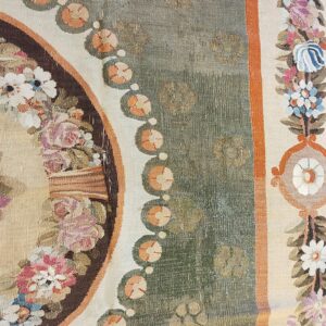 Detail of a rug showing a sage green patterned field and a border with multicolored floral sprays.