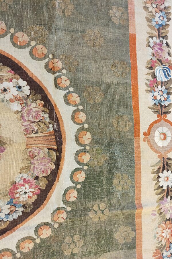 Detail of a rug showing a sage green patterned field and a border with multicolored floral sprays.
