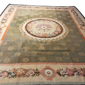 Ornate green rug with repeating floral motifs, a large center medallion, and wide borders of colorful floral garlands.