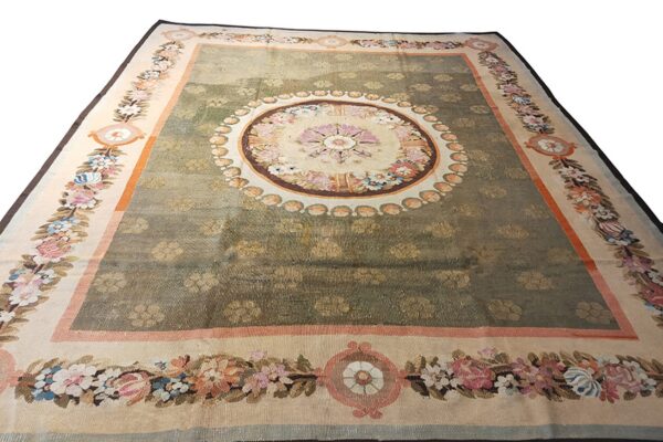 Ornate green rug with repeating floral motifs, a large center medallion, and wide borders of colorful floral garlands.