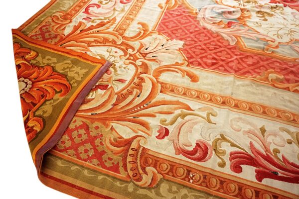 Ornate cream, orange, and red rug with scrolling botanical and geometric border designs in a close-up shot.