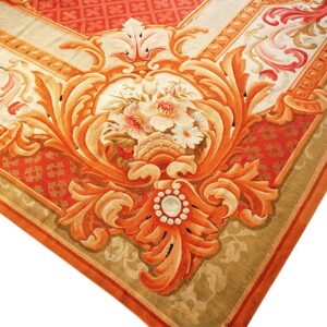Ornate low-pile rug corner featuring detailed red and orange scrolling motifs and a central floral bouquet.