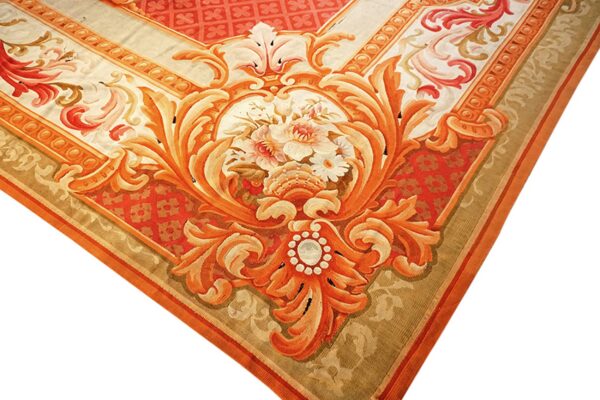 Ornate low-pile rug corner featuring detailed red and orange scrolling motifs and a central floral bouquet.