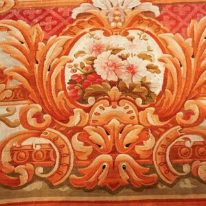 Detailed view of a low-pile rug with terracotta scrolling foliage around a central pink and white floral motif.