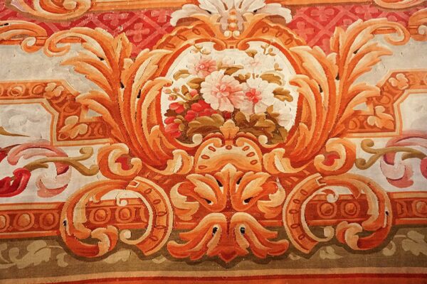 Detailed view of a low-pile rug with terracotta scrolling foliage around a central pink and white floral motif.