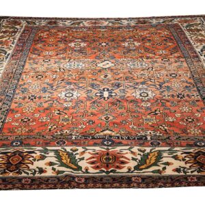 A traditional rug featuring an intricate orange, blue, and cream floral medallion pattern on a white background.