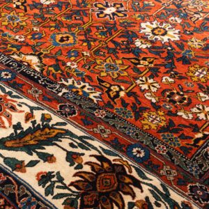 Rust and cream rug close-up with detailed floral patterns in blue, yellow, and green.