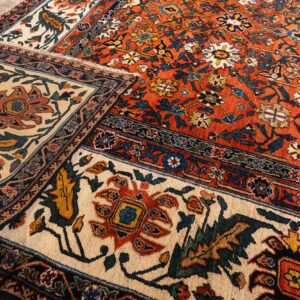 Floral patterned rug with an orange field and wide ivory border folded on weathered wood flooring.