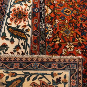 Detailed view of a thick, rust-red and cream floral rug folded on light wood floors.