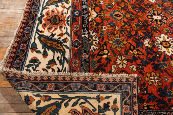 Detailed view of a thick, rust-red and cream floral rug folded on light wood floors.