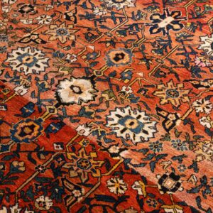 Angled view of a rust-colored rug with complex navy, cream, and gold traditional floral designs.