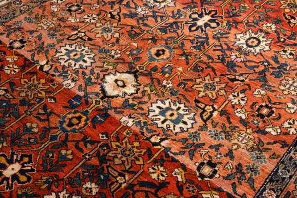 Angled view of a rust-colored rug with complex navy, cream, and gold traditional floral designs.