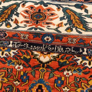 Ornate high-detail rug showing rust, cream, and blue borders, a dense floral pattern, and calligraphic script.