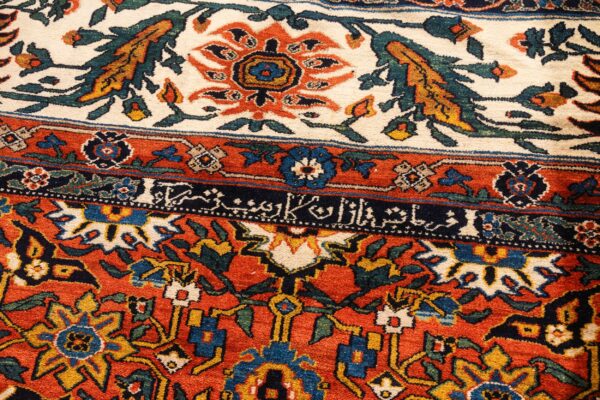 Ornate high-detail rug showing rust, cream, and blue borders, a dense floral pattern, and calligraphic script.