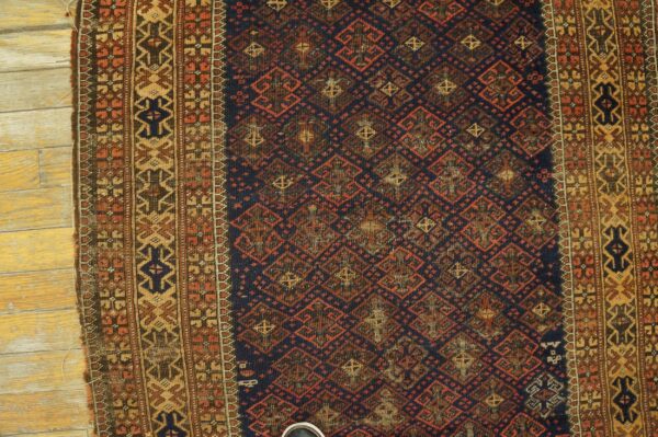 Dark blue rug with rust diamond lattice and wide geometric borders rests on light-colored wood flooring.