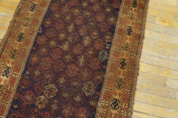 A navy blue runner rug with red and gold geometric patterns rests on distressed light wood floors.