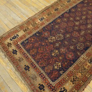 Dark blue rug with rust and gold geometric patterns rests on distressed light wood floorboards.