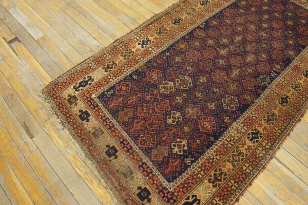 Dark blue rug with rust and gold geometric patterns rests on distressed light wood floorboards.