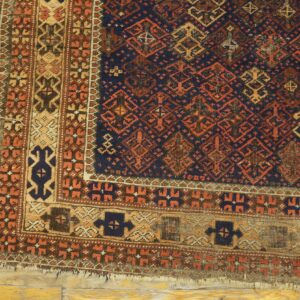 Geometric dark blue and rust rug corner with wide borders rests upon distressed yellow hardwood flooring.
