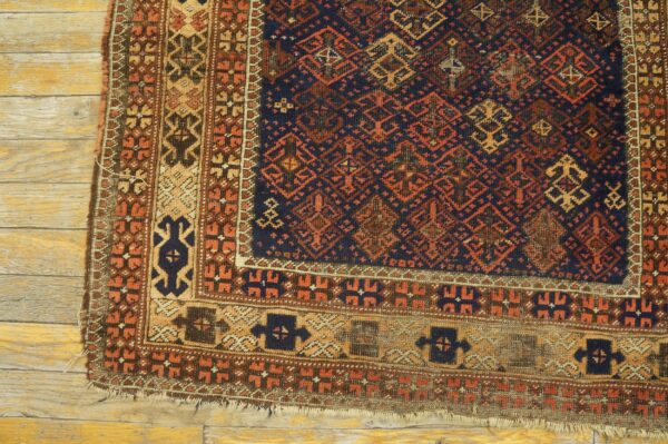 Geometric dark blue and rust rug corner with wide borders rests upon distressed yellow hardwood flooring.