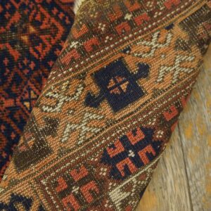 Geometric patterned rug in rust and dark blue curled on rustic wood planks, showing the woven backing.