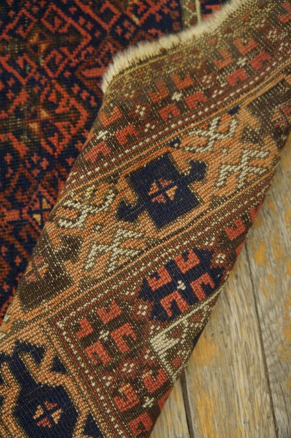 Geometric patterned rug in rust and dark blue curled on rustic wood planks, showing the woven backing.