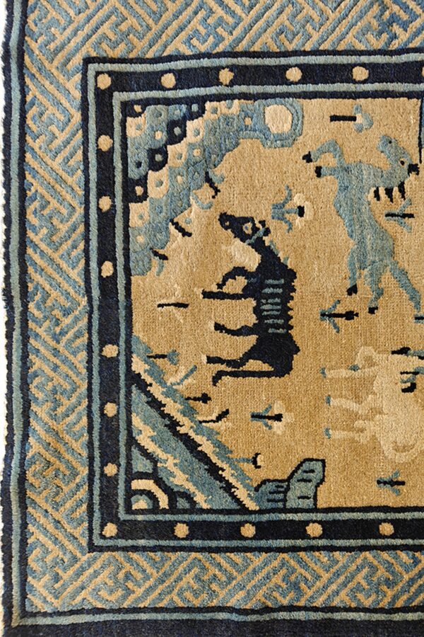 Tan rug detail features dark and light blue figures, surrounded by geometric key and dotted borders.