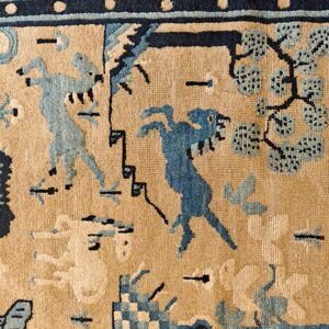 Tan rug with medium pile featuring navy and light blue figures, trees, and geometric border details.