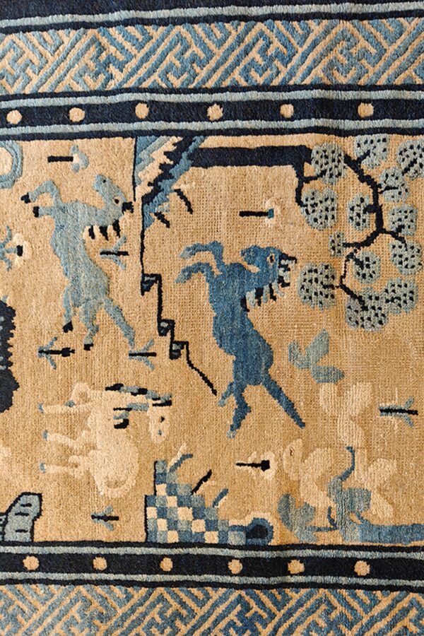 Tan rug with medium pile featuring navy and light blue figures, trees, and geometric border details.