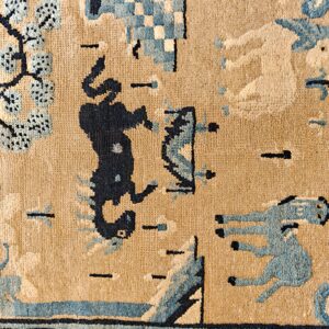 Detail of a low-pile tan rug with blue stylized horses, trees, and dark blue patterned geometric borders.